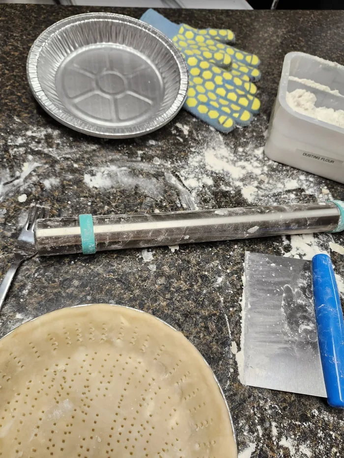 A pie tin, rolling pin and pastry mid-make on the counter