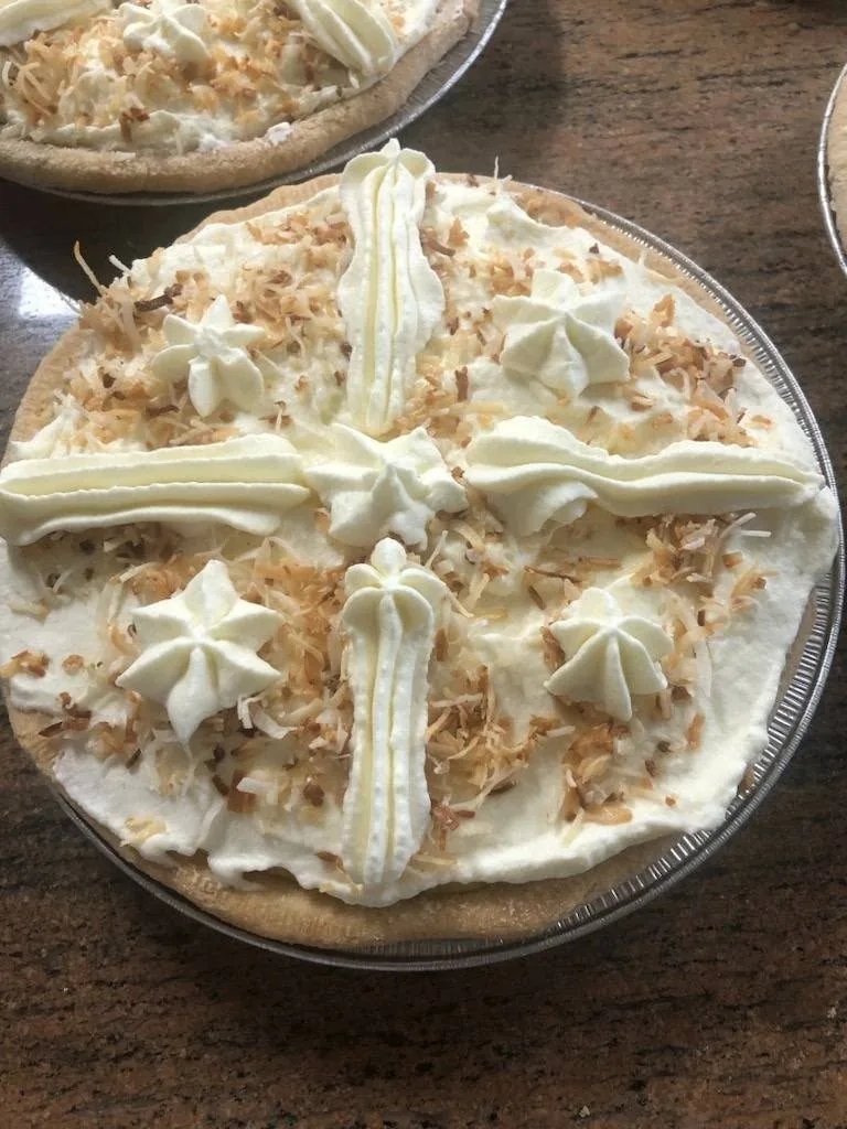 A coconut cream pie topped with piped cream and toasted coconut